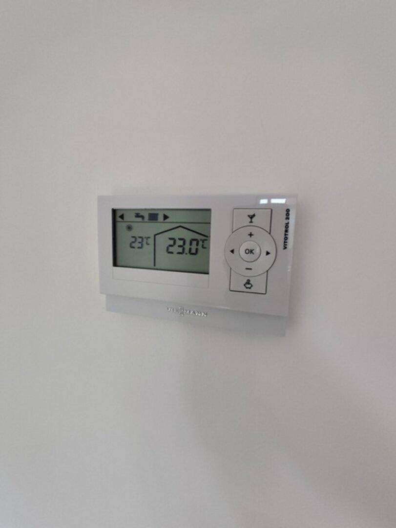 Modernes Thermostat zur Steuerung der Raumtemperatur an einer weißen Wand montiert.