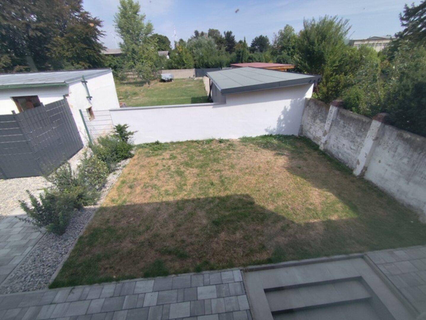 Kleiner Gartenbereich mit Rasenfläche und gepflastertem Zugang, umgeben von Mauern.
