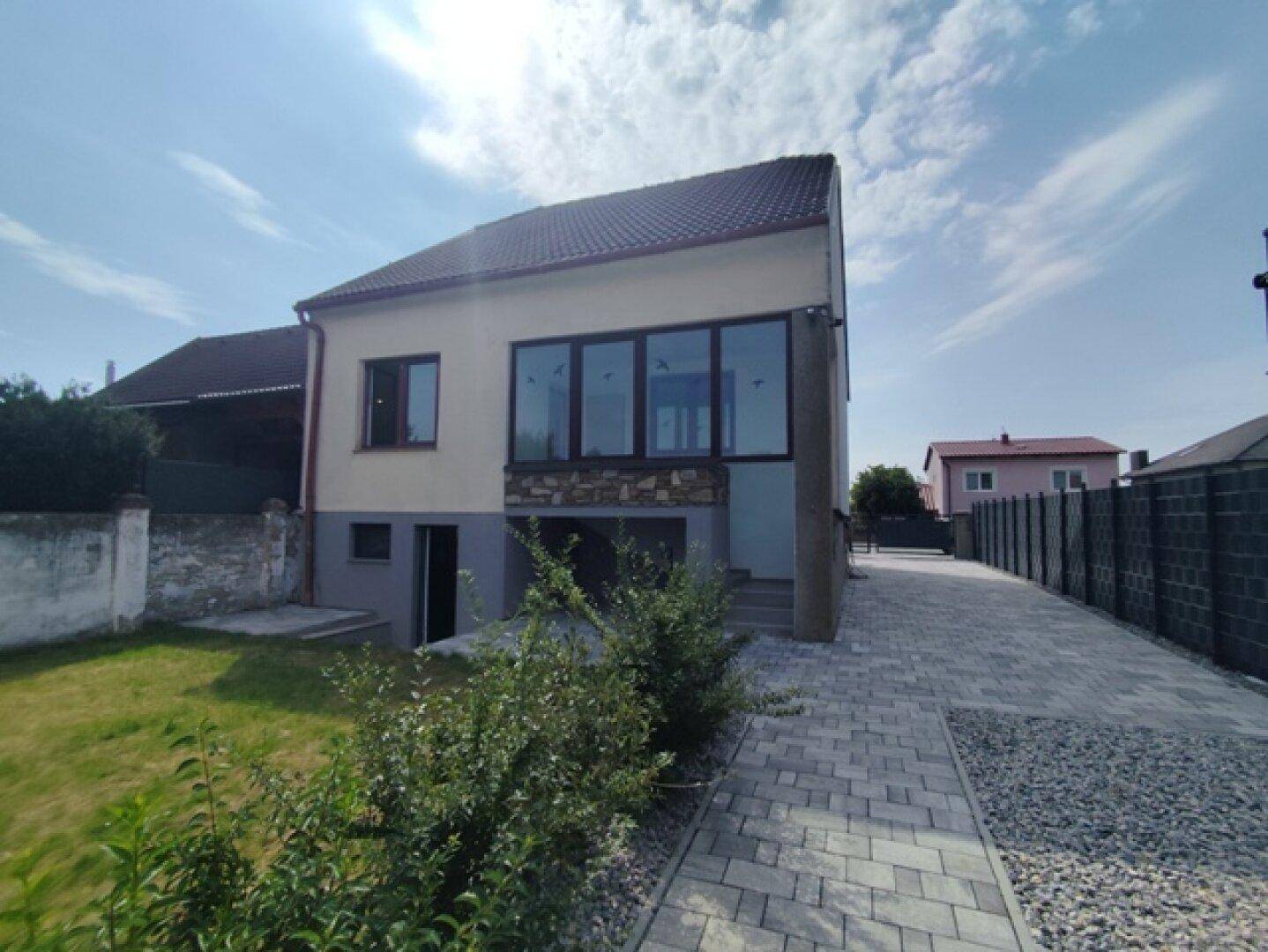 Seitenansicht eines modernen Hauses mit großen Fenstern und gepflastertem Zugangsbereich.