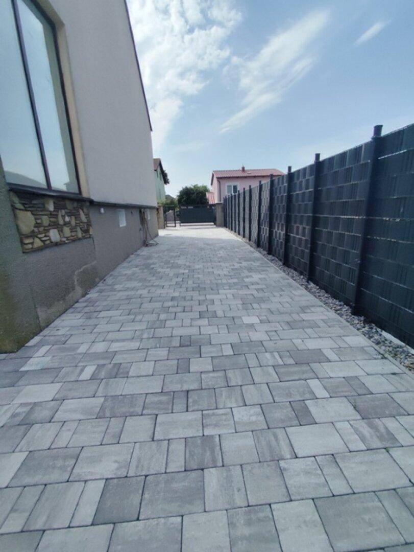 Lange, gepflasterte Zufahrt zum Haus, umgeben von einem modernen Sichtschutzzaun.