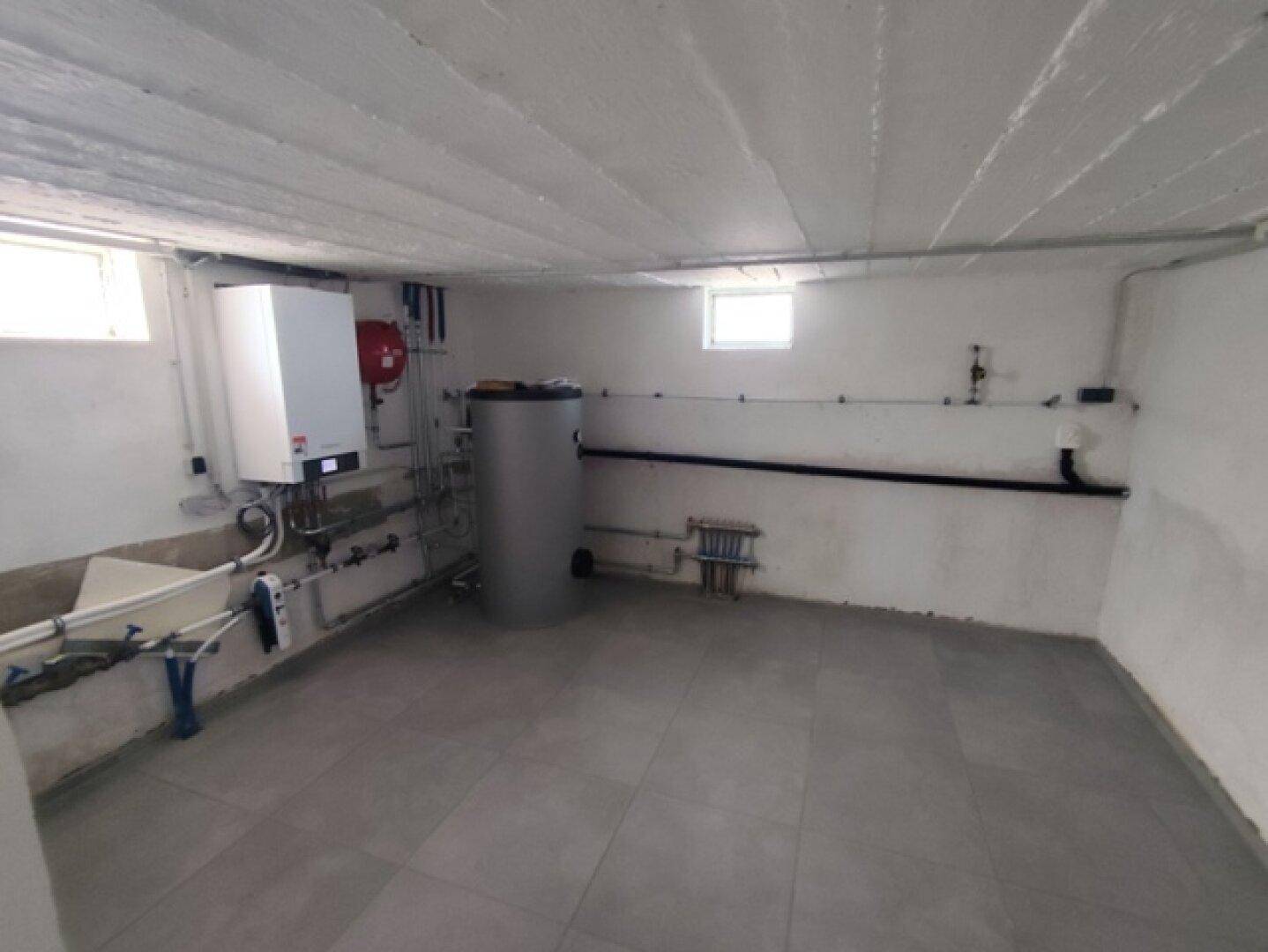 Heller und sauberer Hauswirtschaftsraum mit moderner Heizungsanlage, Warmwasserspeicher und kleinen Fenstern.