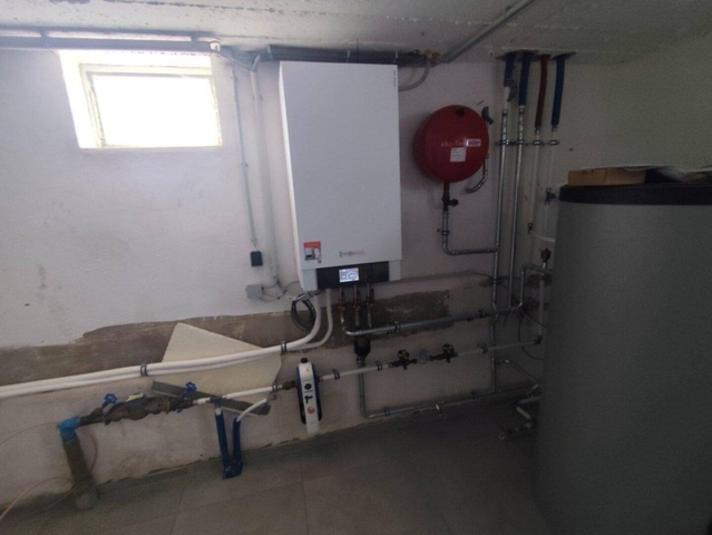 Detailansicht der modernen Heizungsanlage und des Warmwasserspeichers im Hauswirtschaftsraum mit Fenster.
