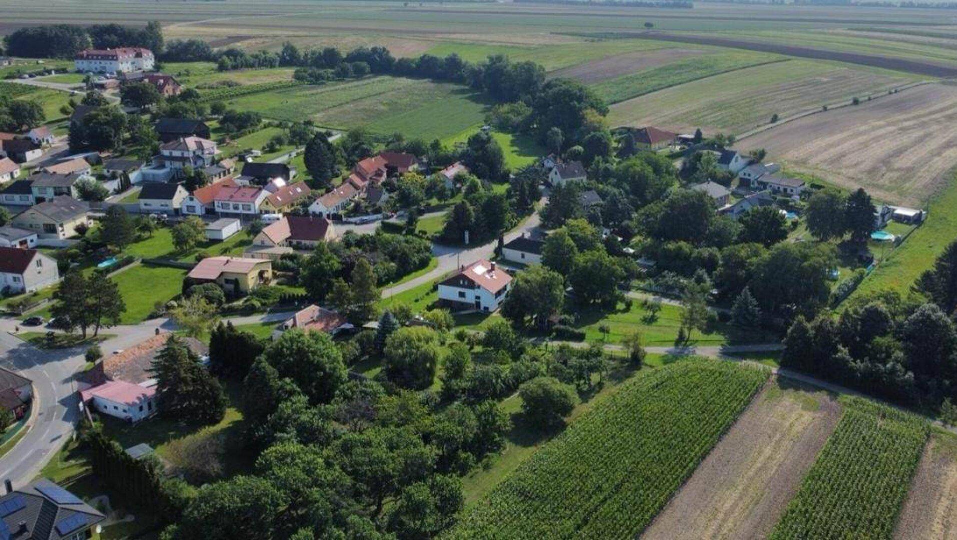 Weitläufige Luftaufnahme einer ländlichen Siedlung mit Häusern, Feldern und viel Grün.