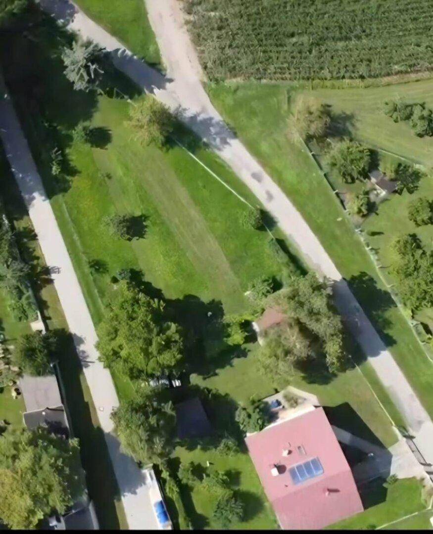 Luftaufnahme von oben mit Straßen, grünen Flächen und einem Haus mit rotem Dach.