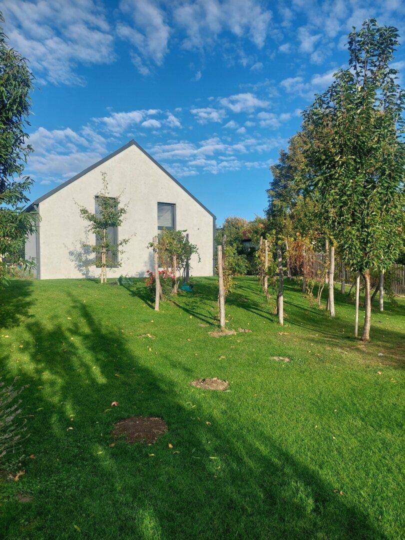 Modernes weißes Einfamilienhaus mit Giebeldach, umgeben von einer großen Rasenfläche.