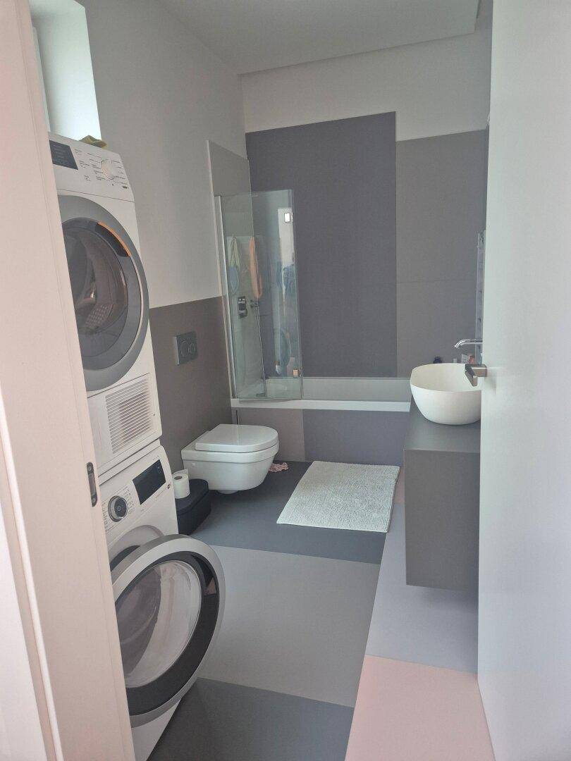 Modernes Badezimmer mit Dusche, Toilette, Waschbecken und integrierter Waschmaschine.