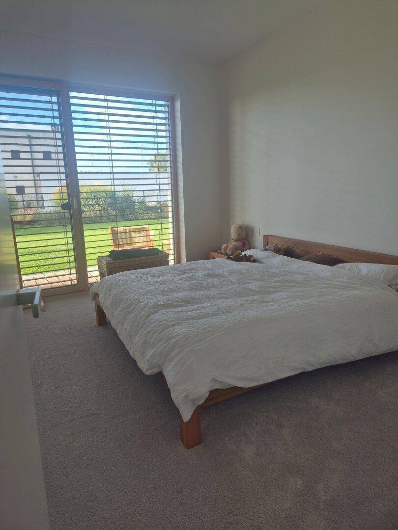 Schlafzimmer mit Teppichboden, großem Fenster und Blick ins Grüne.