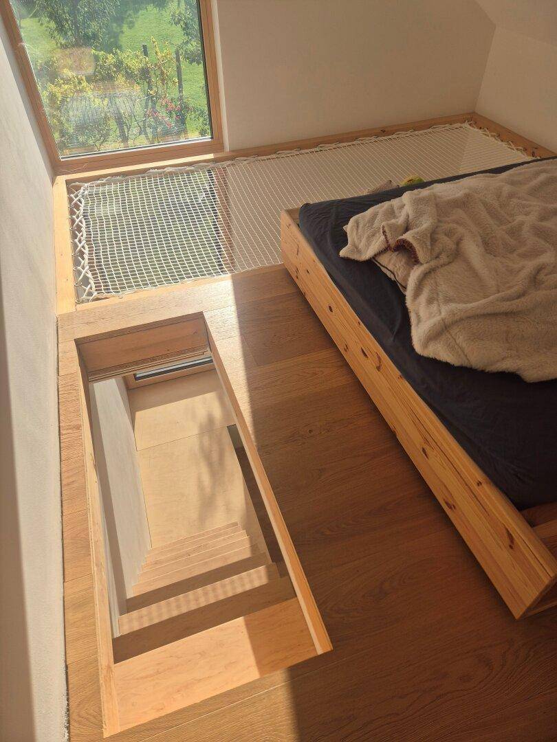 Schlafbereich mit Holzbett, integrierter Treppe und großem Fenster mit Blick ins Grüne.