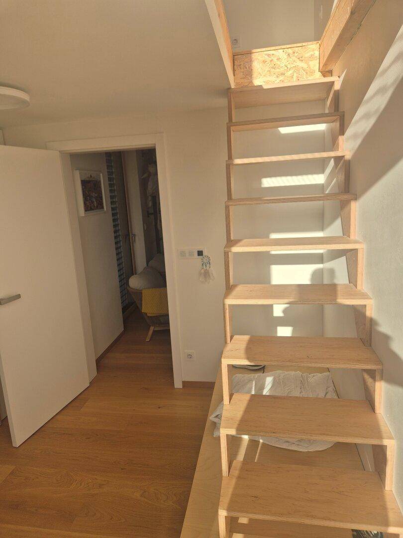 Helle Holztreppe führt in den oberen Bereich, mit weißer Tür und Holzfußboden.