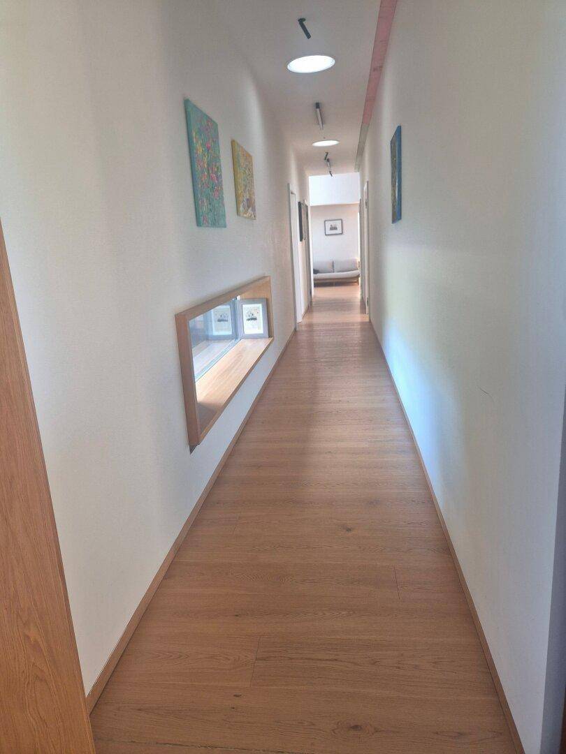 Langer, heller Flur mit Holzboden und integrierten Lichtelementen.