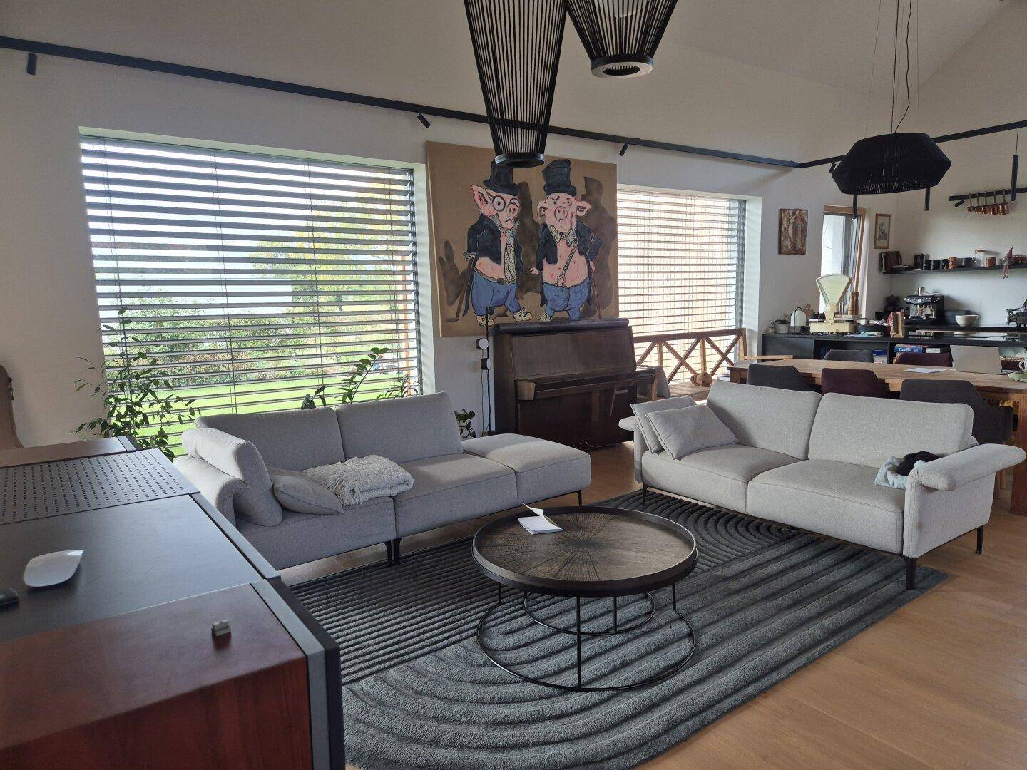 Heller Wohnbereich mit bequemen Sofas, Holzboden und großen Fenstern.