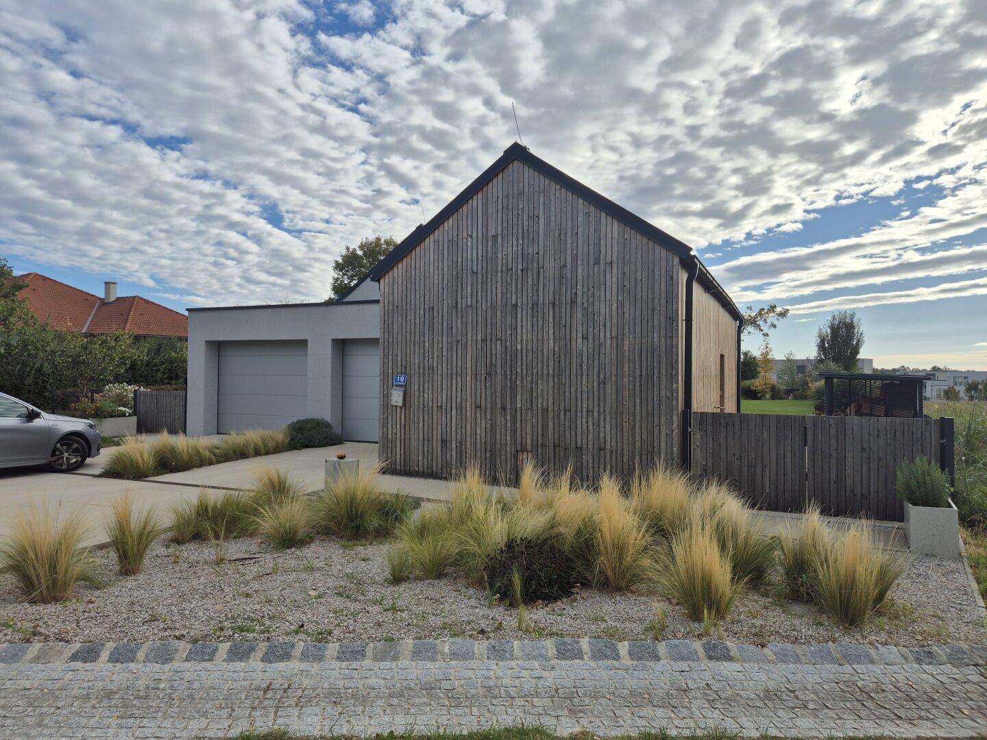 Seitenansicht des modernen Hauses mit Holzfassade und gepflegtem Vorgarten.