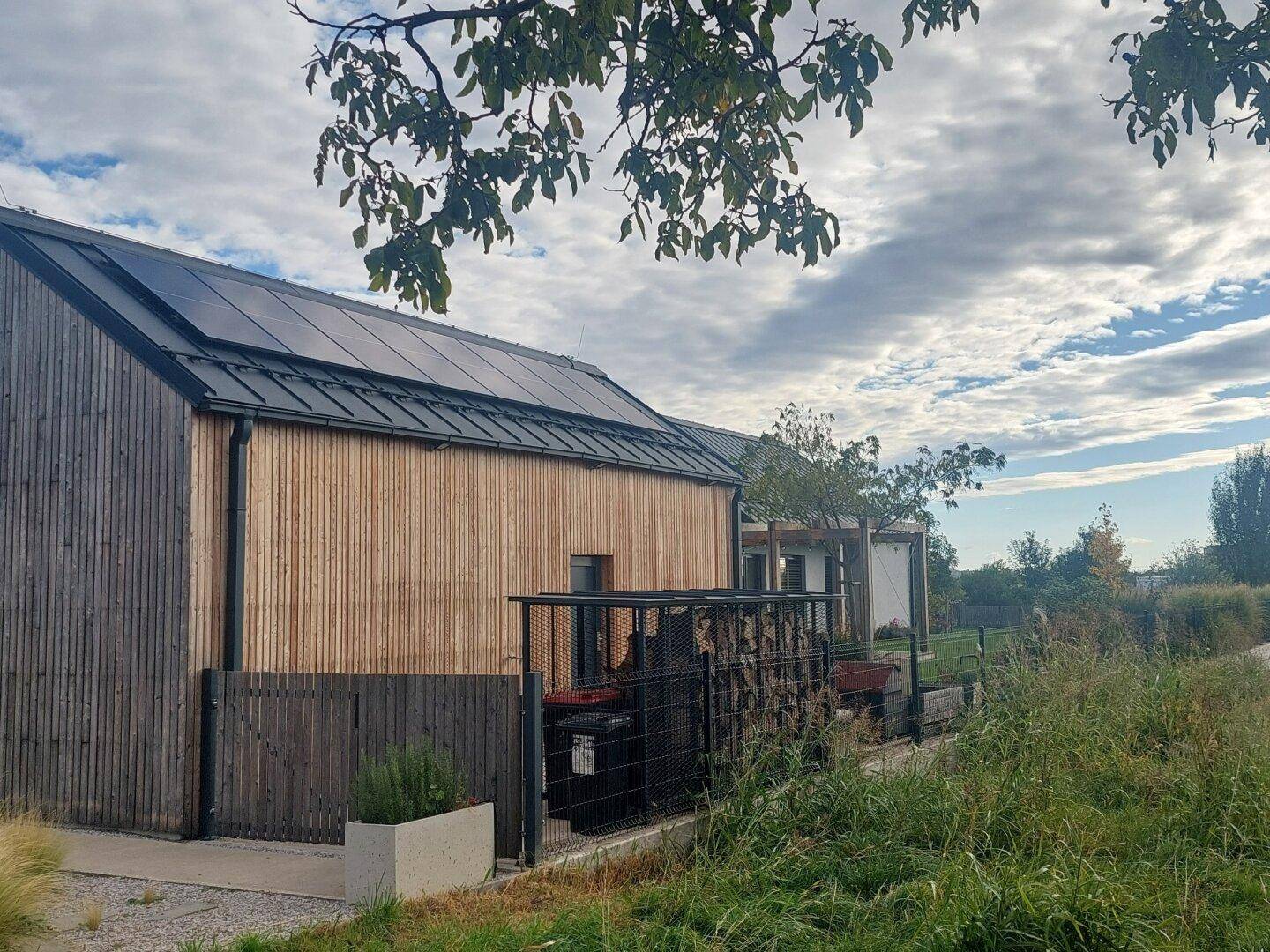 Detailansicht der Photovoltaikanlage auf dem Dach und der Holzfassade des Hauses.