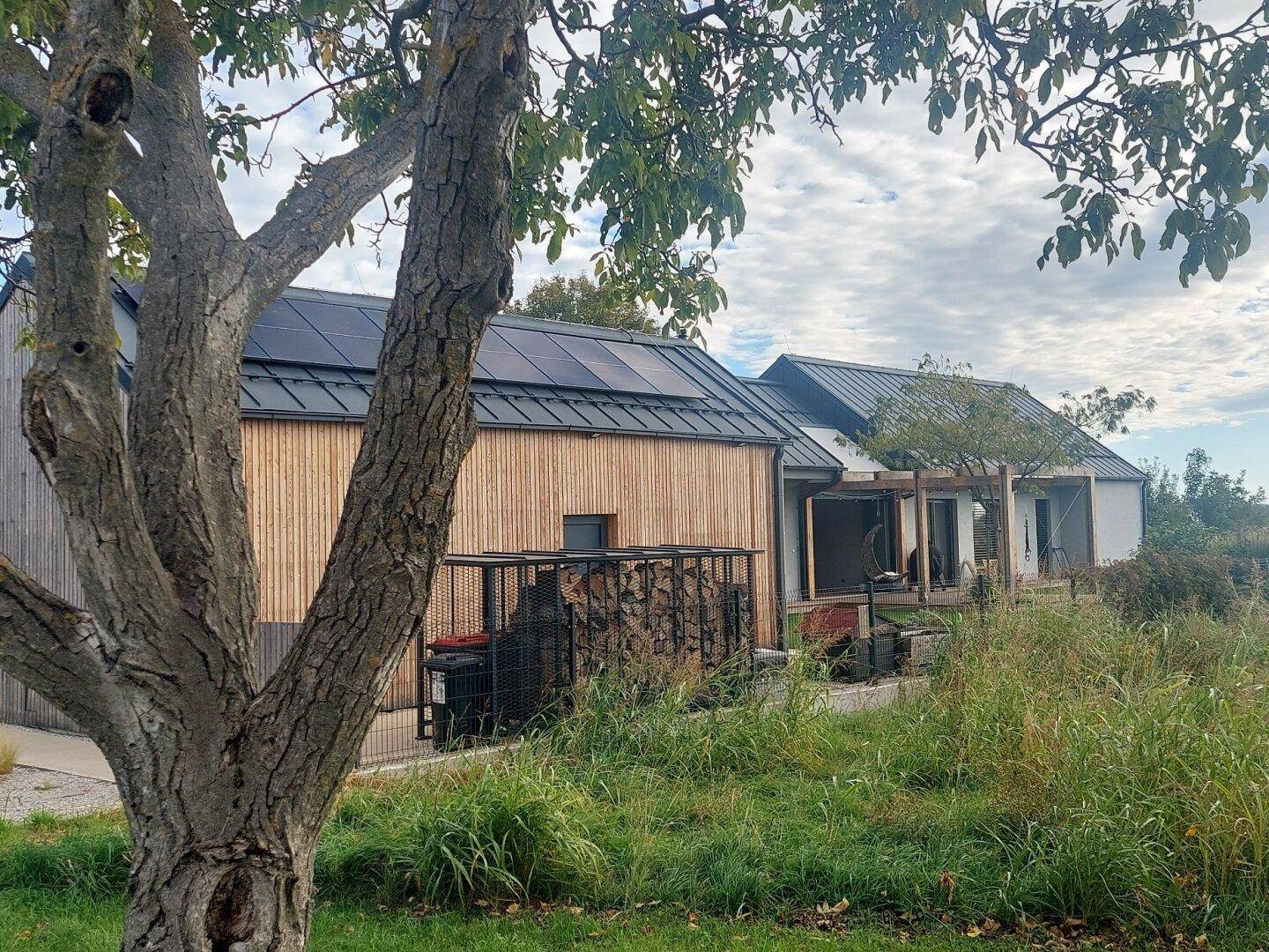 Modernes Haus mit Holzfassade, Solaranlage auf dem Dach und Holzstapel.