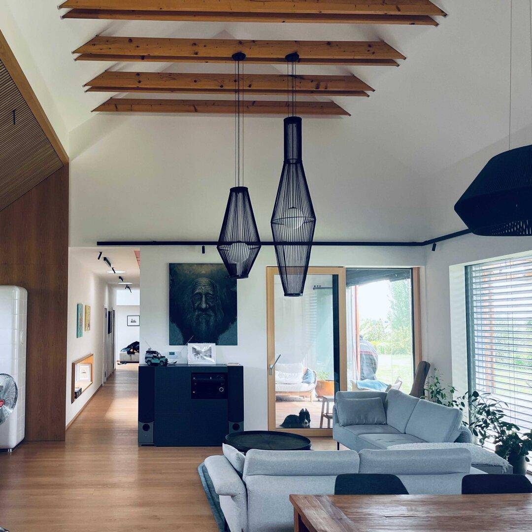 Geräumiges Wohnzimmer mit hohen Decken, Holzbalken und Blick ins Grüne.