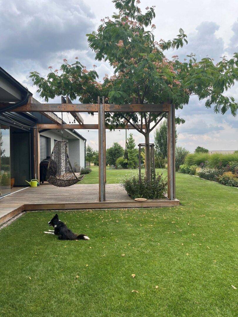 Moderner Gartenbereich mit Holzterrasse, Pergola und großzügiger Rasenfläche.