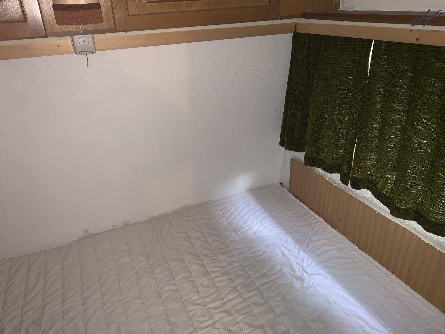 Einfaches Schlafzimmer in einem Wohnwagen mit Matratze und dunklen Vorhängen.