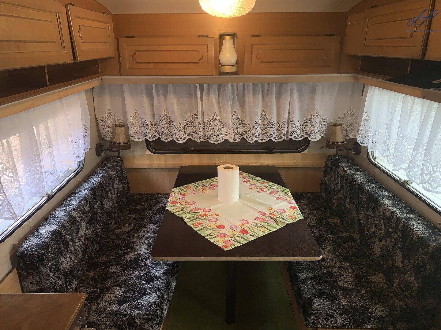 Gemütlicher Wohn-Essbereich in einem Wohnwagen mit floralen Polstern und Vorhängen.