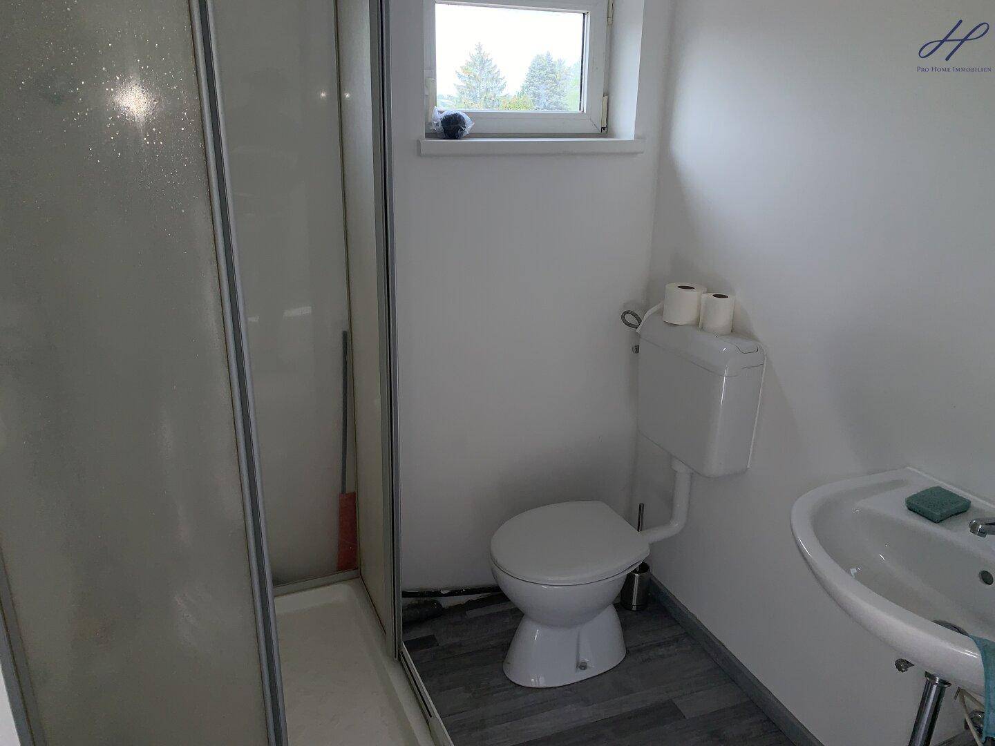 Kleines Badezimmer mit Dusche, Toilette und Waschbecken, ausgestattet mit einem Fenster.