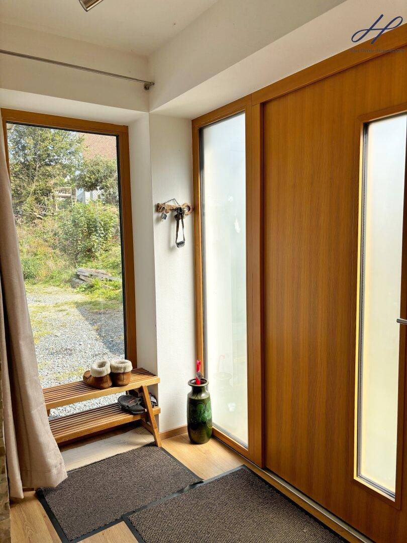 Heller Eingangsbereich mit Holztür, großem Fenster und praktischer Schuhbank.