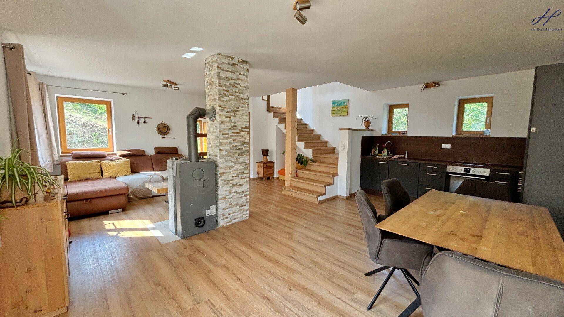 Offener Wohn-Essbereich mit Holzboden, Kaminofen und integrierter Küchenzeile.