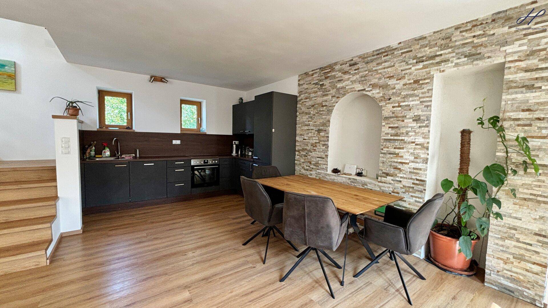 Essbereich mit Holztisch und moderner Küchenzeile, akzentuiert durch eine Steinwand.