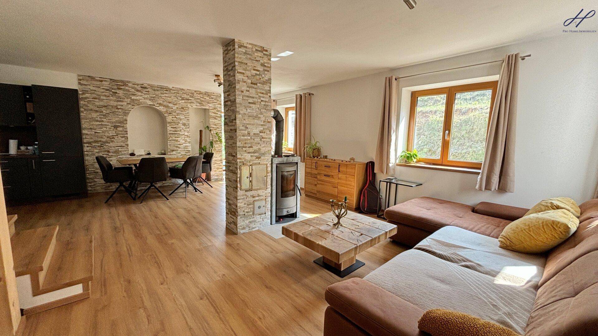 Gemütlicher Wohnbereich mit großem Sofa, Holztisch und Kaminofen, offen zum Essbereich.