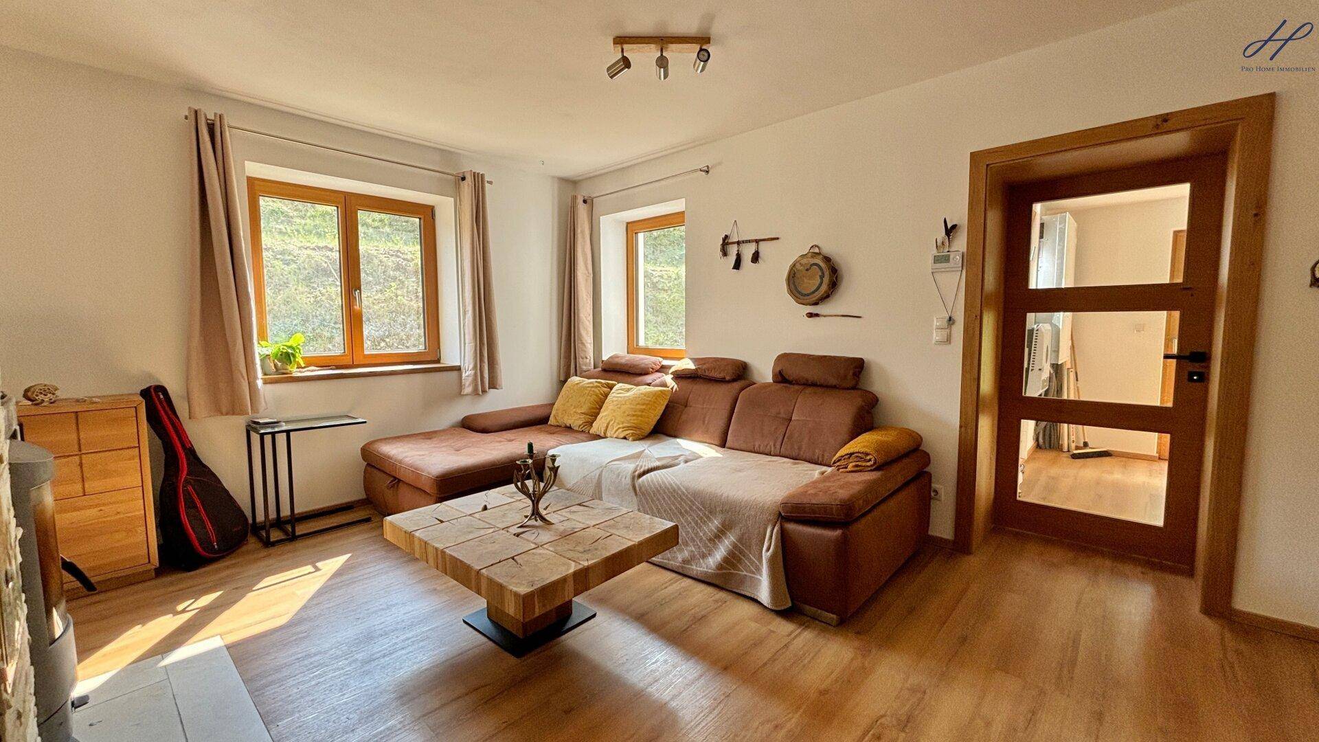 Heller Wohnbereich mit bequemer Couch, Holztisch und Blick ins Grüne durch große Fenster.