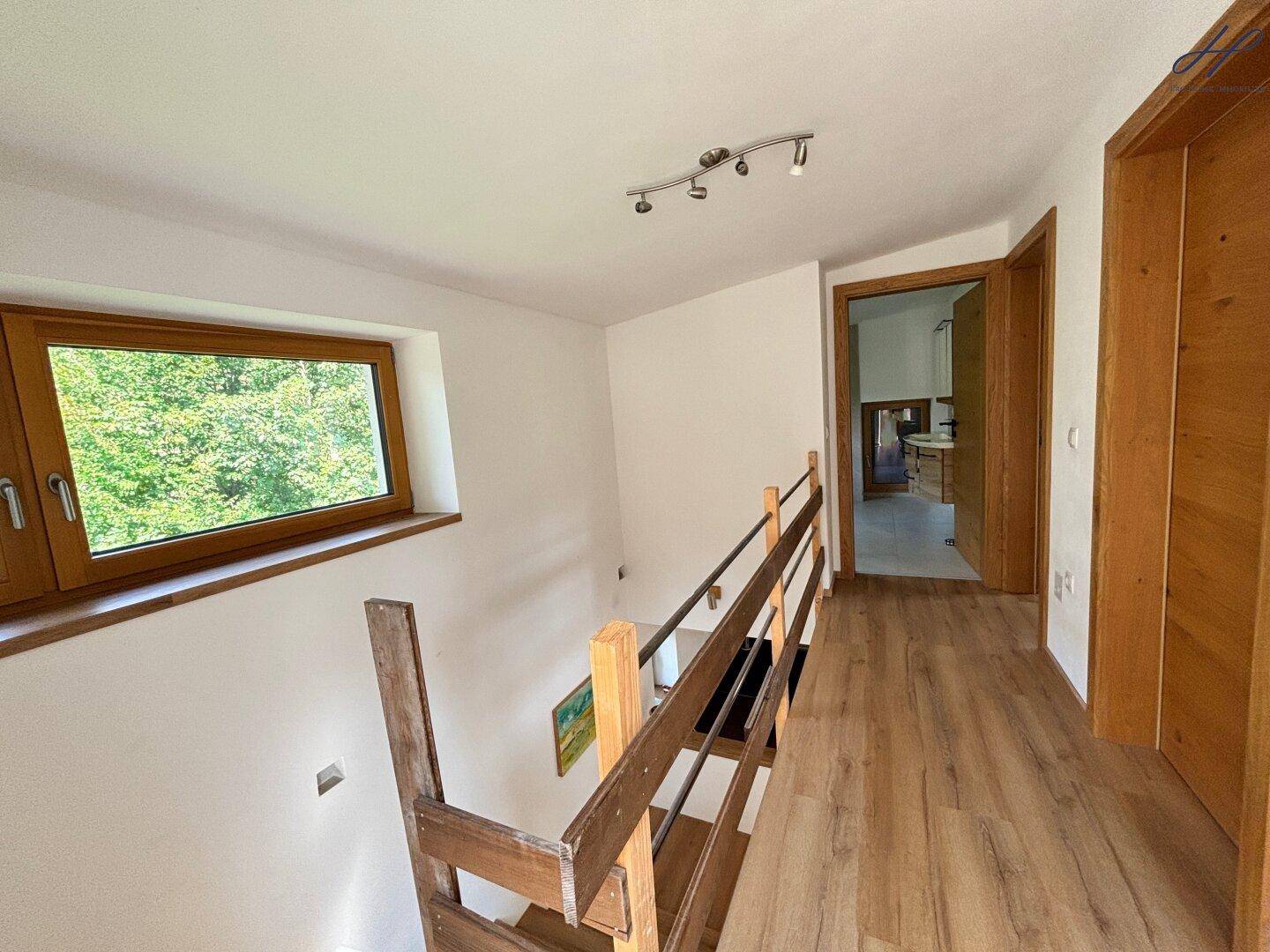 Heller Flur im Obergeschoss mit Holzgeländer und Blick ins Grüne durch das Fenster.