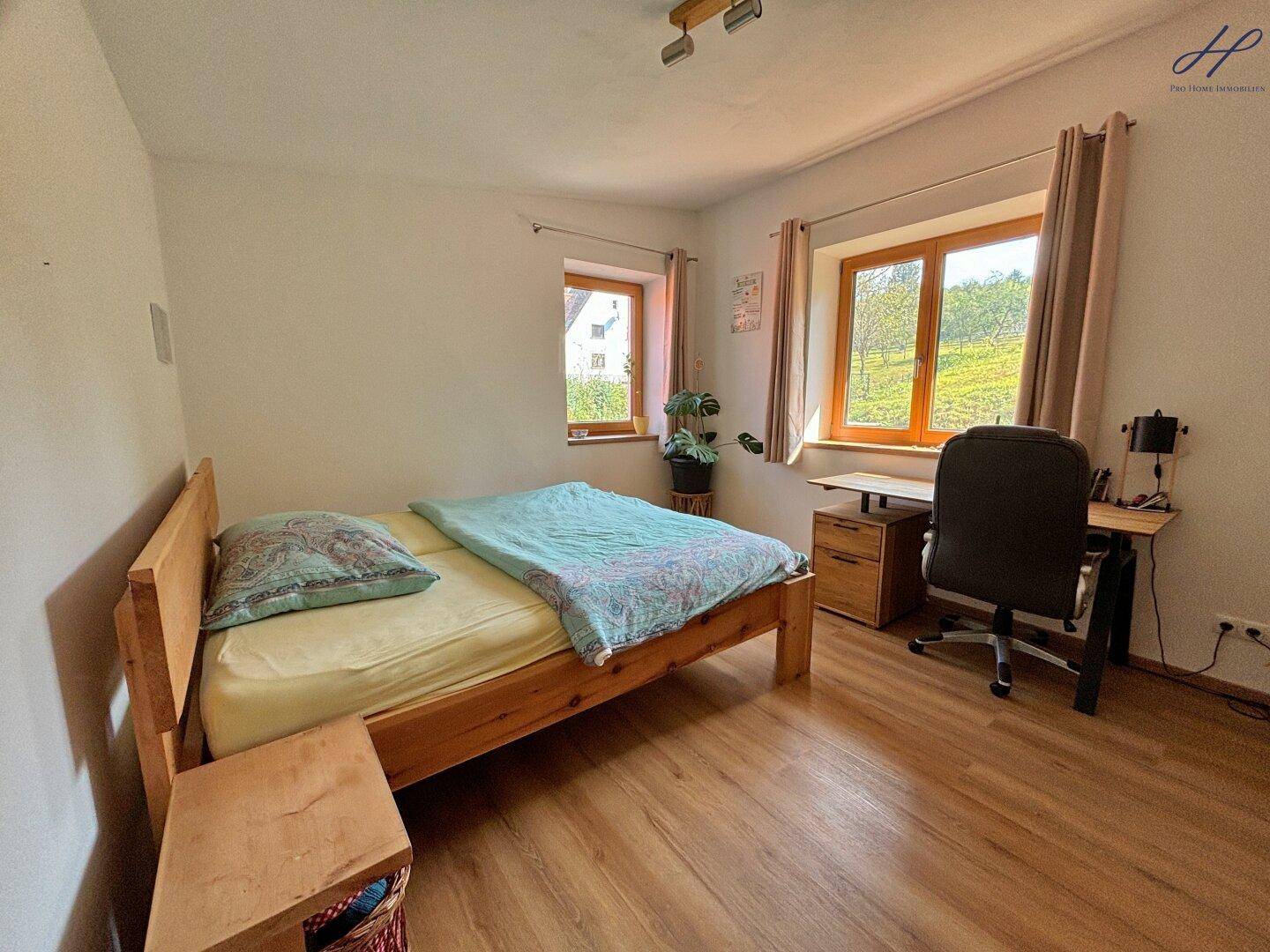 Gemütliches Schlafzimmer mit Holzbett, Schreibtisch und Blick auf die grüne Landschaft.