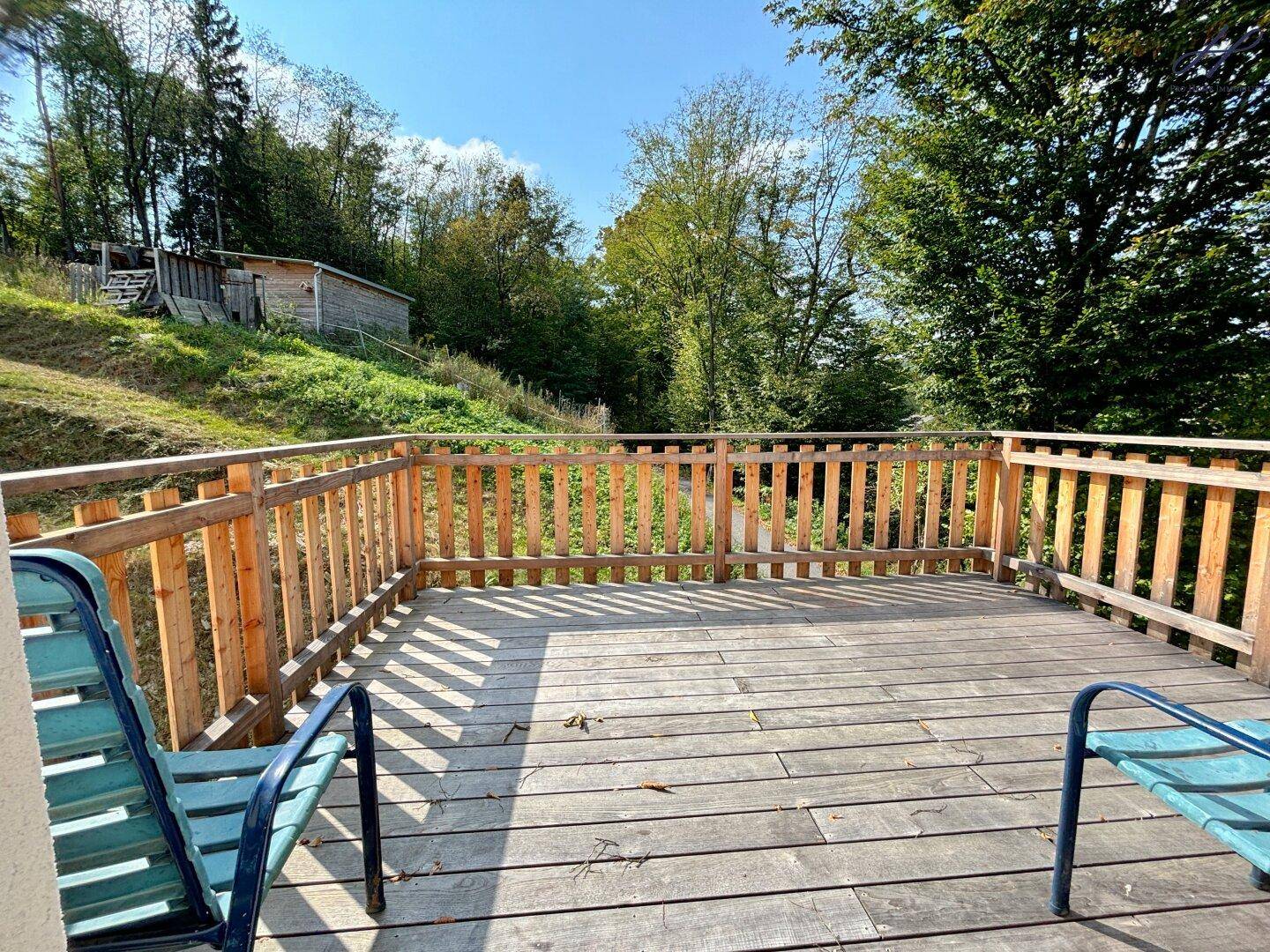 Geräumiger Holzbalkon mit Sitzgelegenheiten und weitem Blick auf die grüne Umgebung.