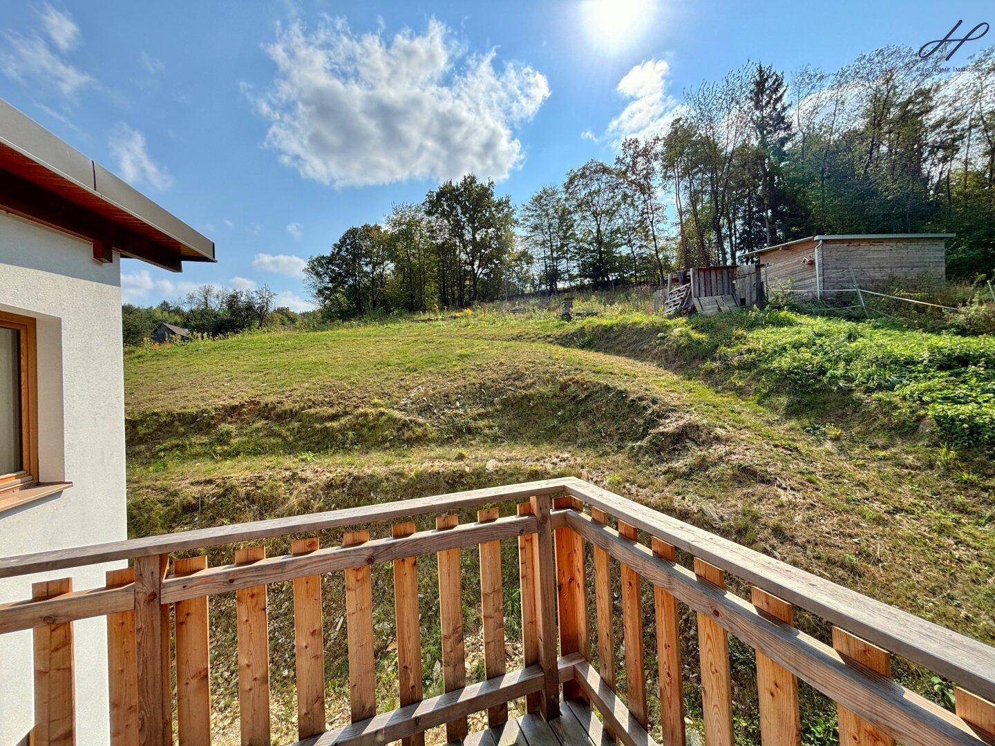 Sonniger Holzbalkon mit Blick auf die weitläufige grüne Hügellandschaft unter blauem Himmel.