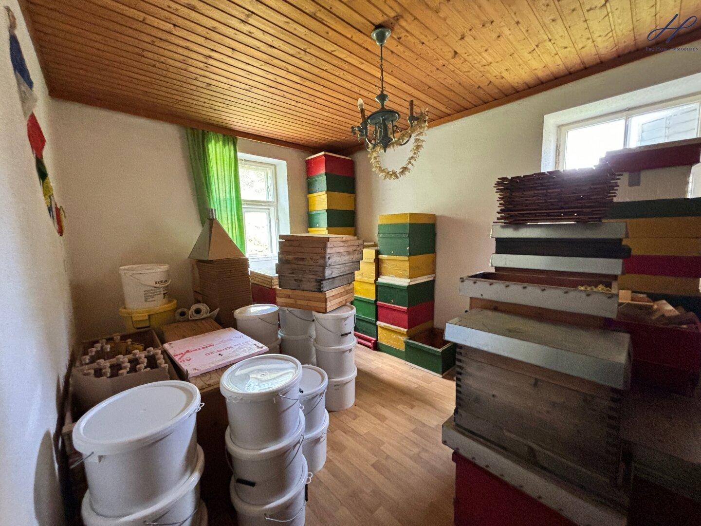Lagerraum mit Holzbalkendecke und gestapelten Bienenstöcken und Eimern.