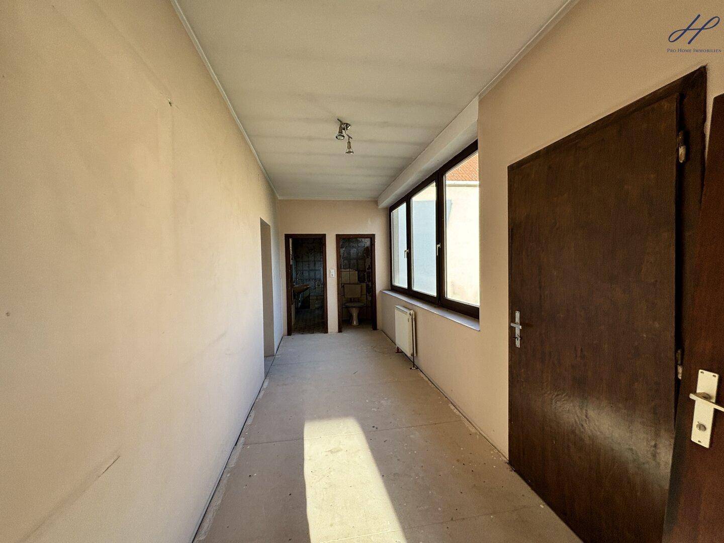 Heller Flur mit Fenster, kahlen Wänden und mehreren Türen.