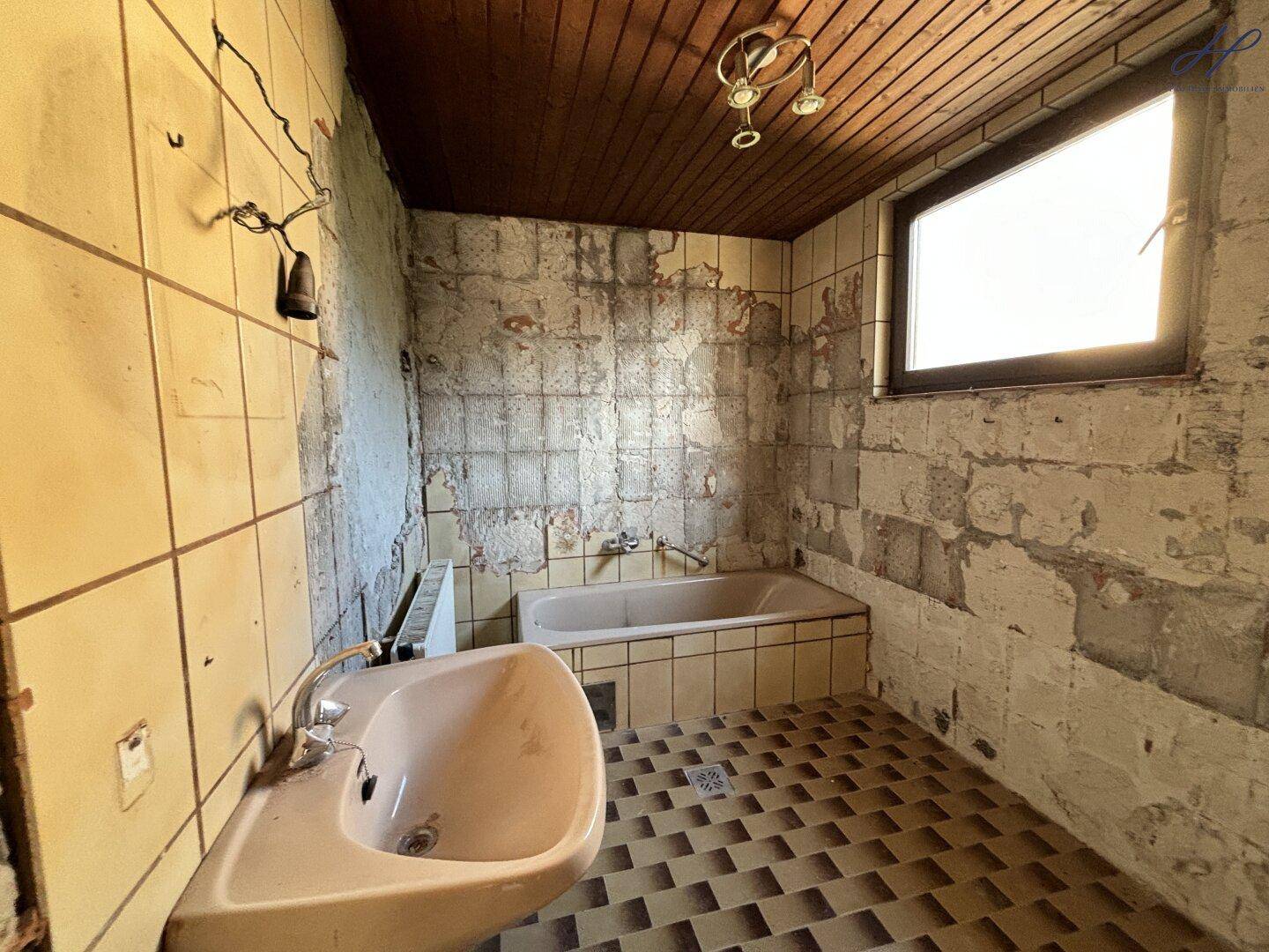 Badezimmer im Renovierungszustand mit alter Badewanne, Waschbecken und Fliesen.