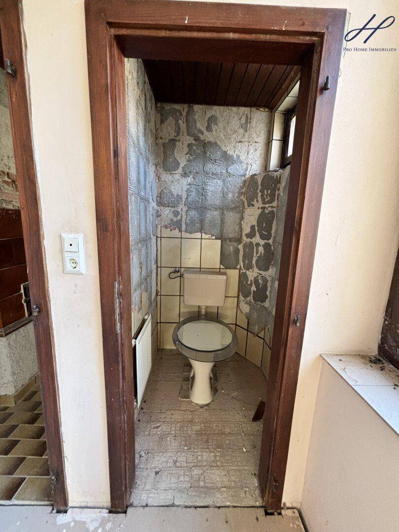 Kleine Toilette im Renovierungszustand mit WC und alten Fliesen.