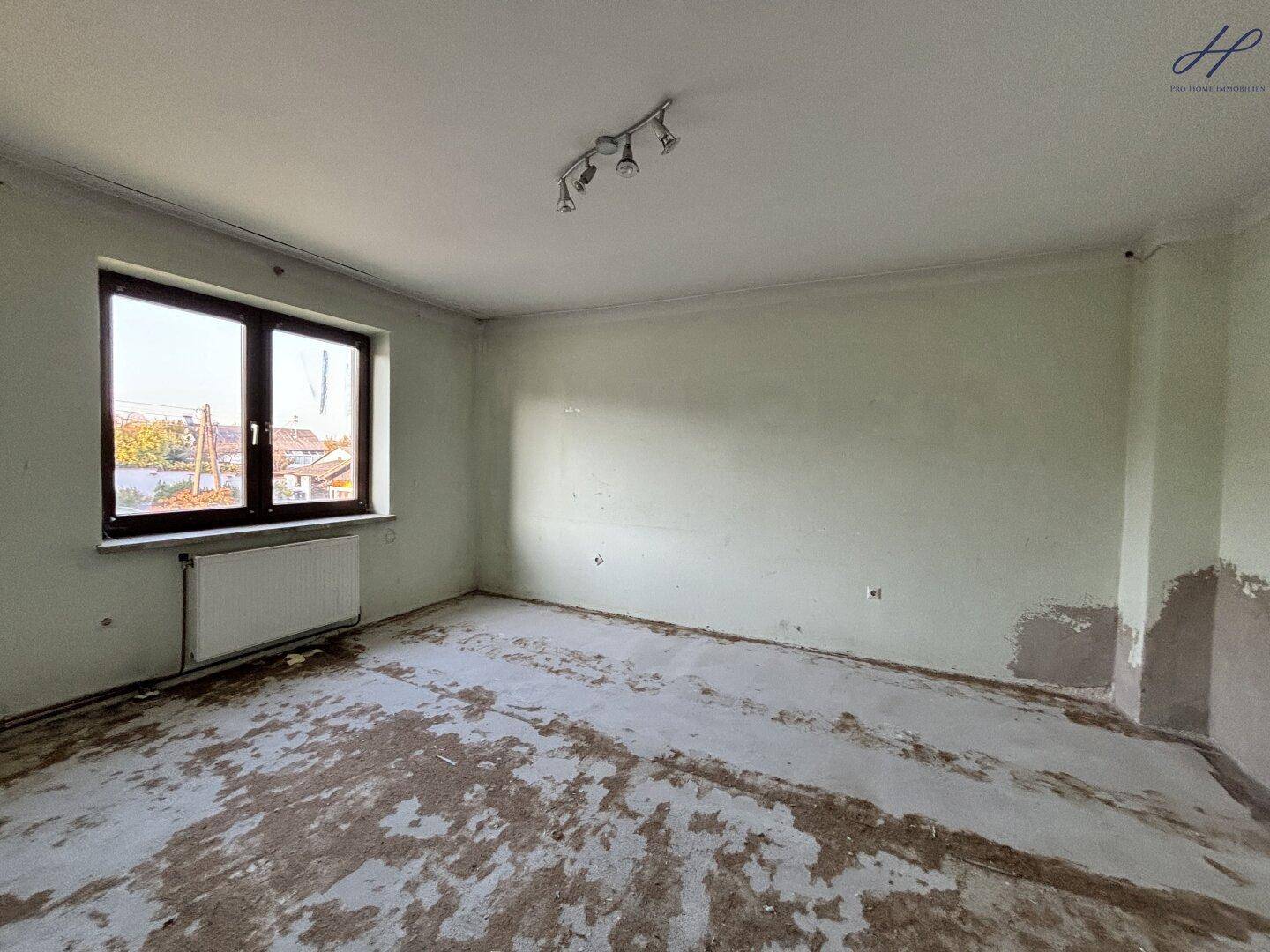 Leerer Raum mit hellgrünen Wänden, einem Fenster und unfertigem Boden.