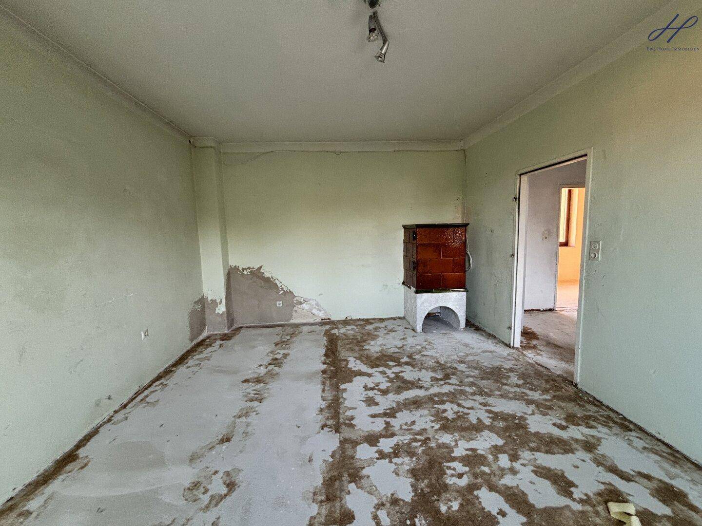 Leerer Raum mit hellgrünen Wänden, einem Fenster und einem Kachelofen.