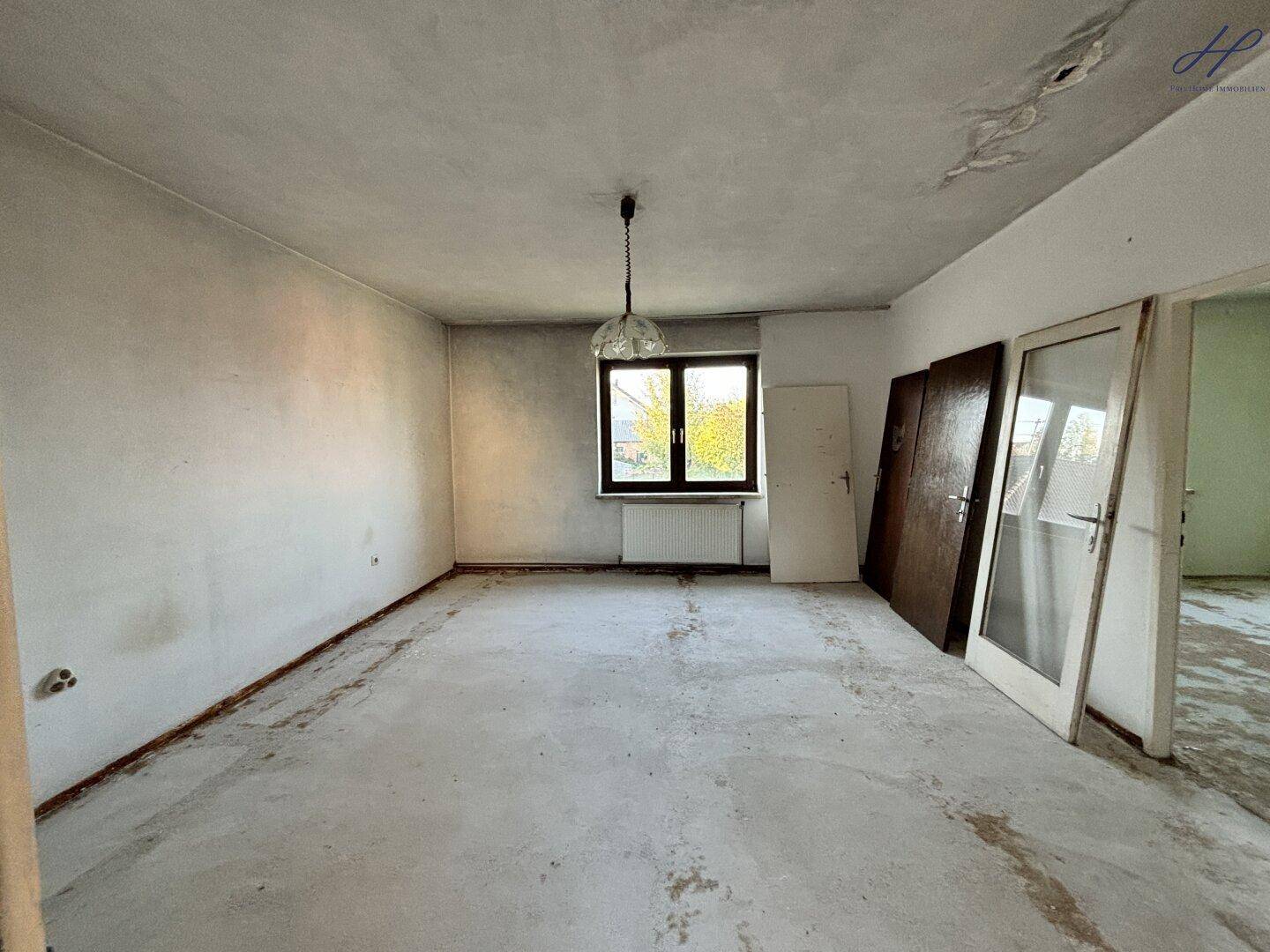 Leerer Raum mit Fenster, unfertigem Boden und Türen, die an der Wand lehnen.