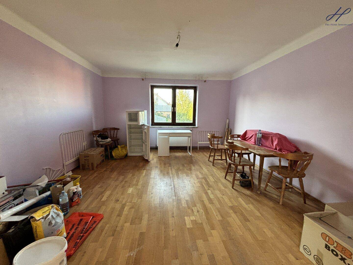 Raum mit lila Wänden, Parkettboden und verschiedenen Gegenständen, die auf einen Umzug hindeuten.