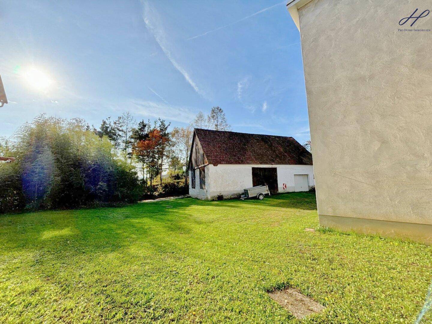 Weitläufiger Gartenbereich mit einem rustikalen Nebengebäude und altem Baumbestand.