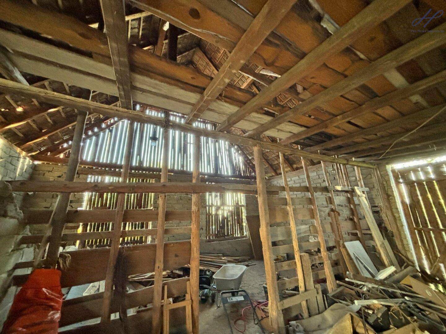 Innenansicht eines alten Scheunengebäudes mit freiliegenden Holzbalken und viel Tageslicht.