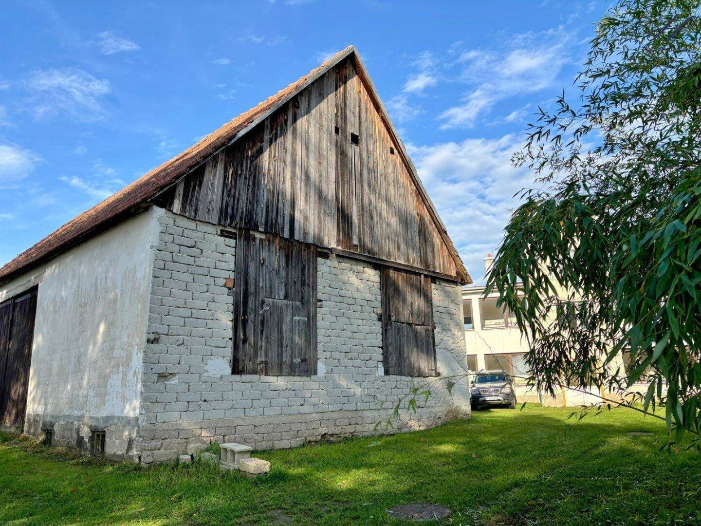 Seitenansicht des rustikalen Nebengebäudes mit Holztüren und Ziegelmauerwerk.