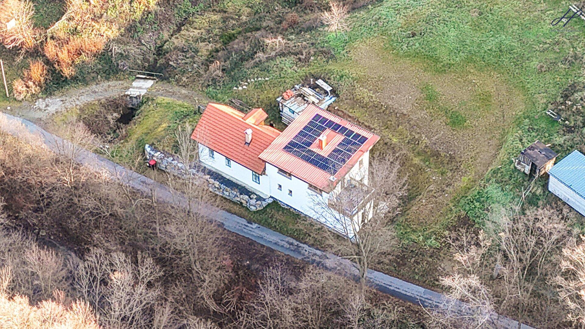 Luftaufnahme des Hauses mit Solaranlage auf dem Dach und angrenzender Straße und Grünflächen.