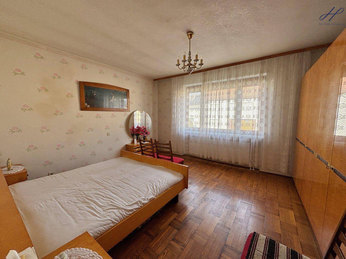 Helles Schlafzimmer mit Parkettboden, Einzelbett und großem Fenster.