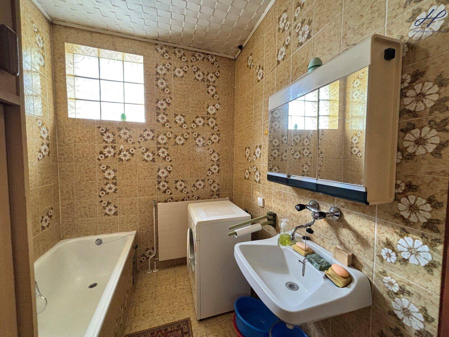 Badezimmer mit Badewanne, Waschbecken und floral gemusterten Fliesen.