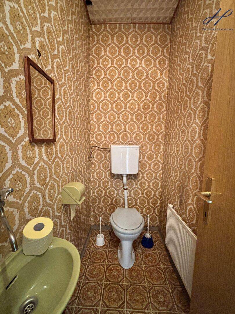 Separate Toilette mit gemusterter Tapete und kleinem Waschbecken.