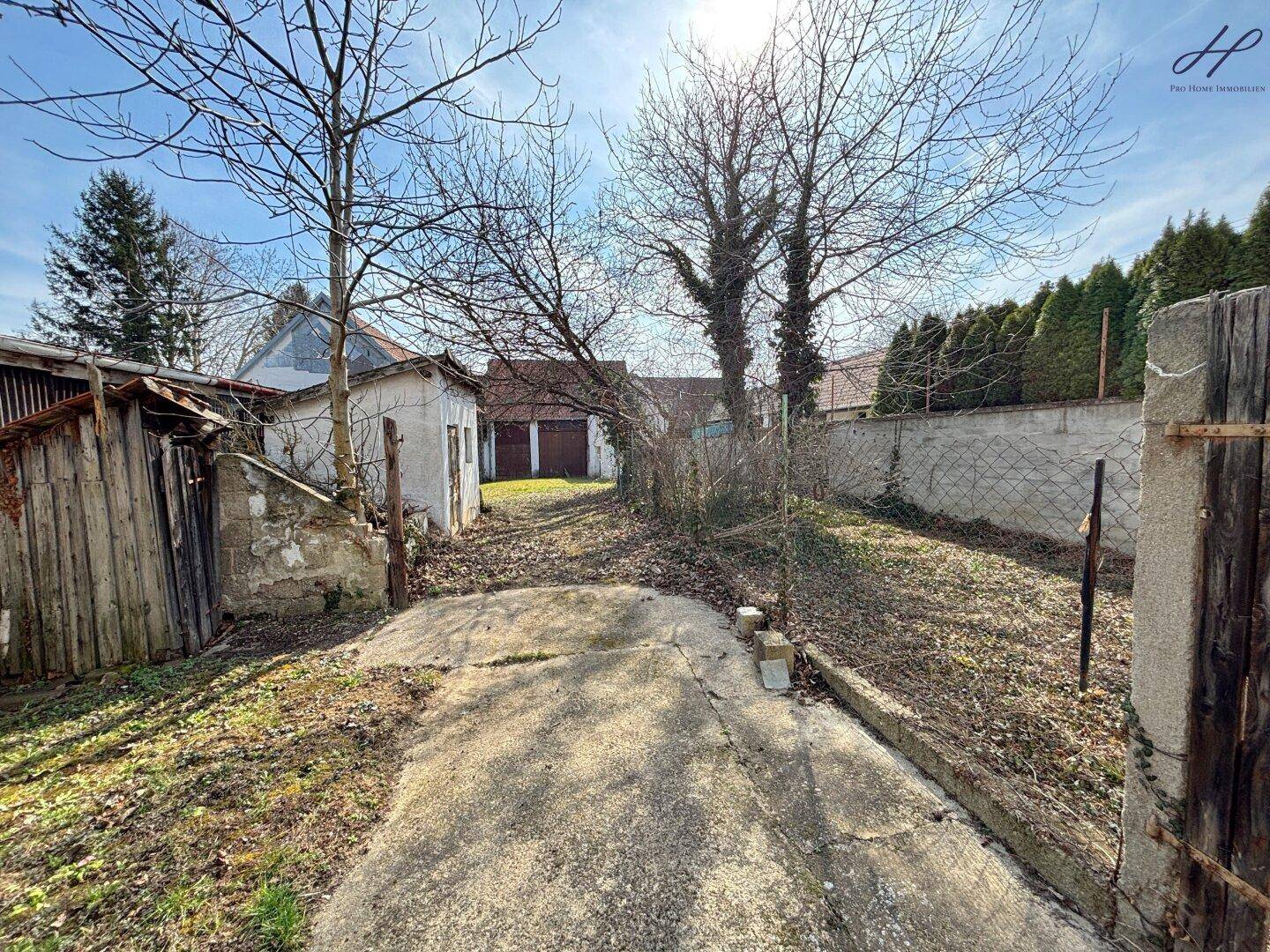 Hinterer Gartenbereich mit Betonweg und Blick auf Garagen.