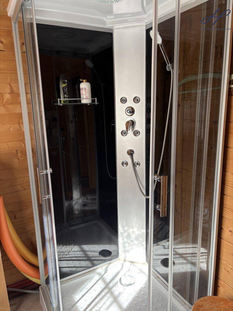 Moderne Duschkabine mit Glaswänden und mehreren Duschköpfen in einem Holzbad.