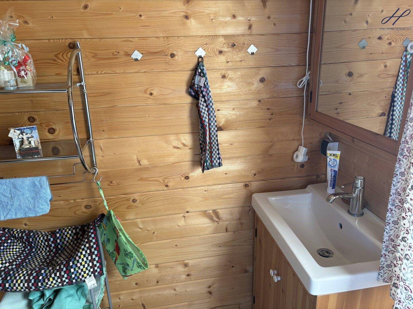 Badezimmer mit Holzwänden, Einzelwaschbecken und Spiegel.